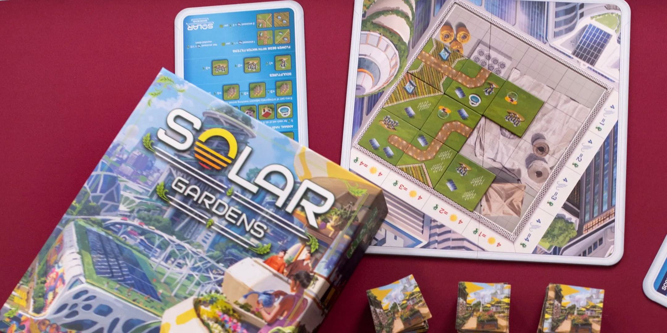 Hộp game và các thành phần của board game Solar Gardens được sắp xếp trên nền đỏ