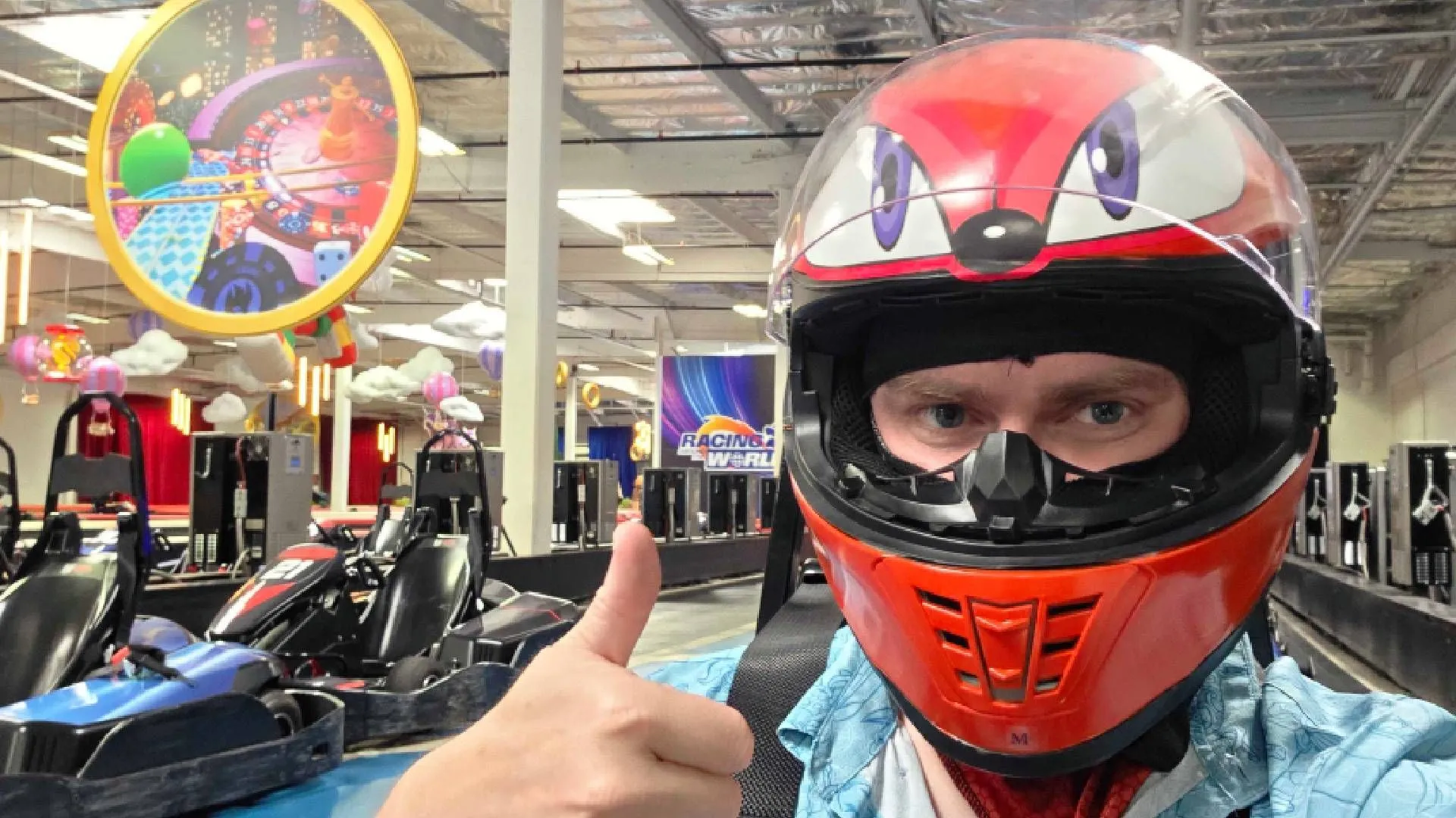 Người chơi giơ ngón cái trên đường đua go-kart chủ đề Sonic Racing: Crossworlds tại K1 Speed, với hình nộm Knuckles bay lơ lửng, thể hiện sự hứng khởi và tinh thần cạnh tranh.